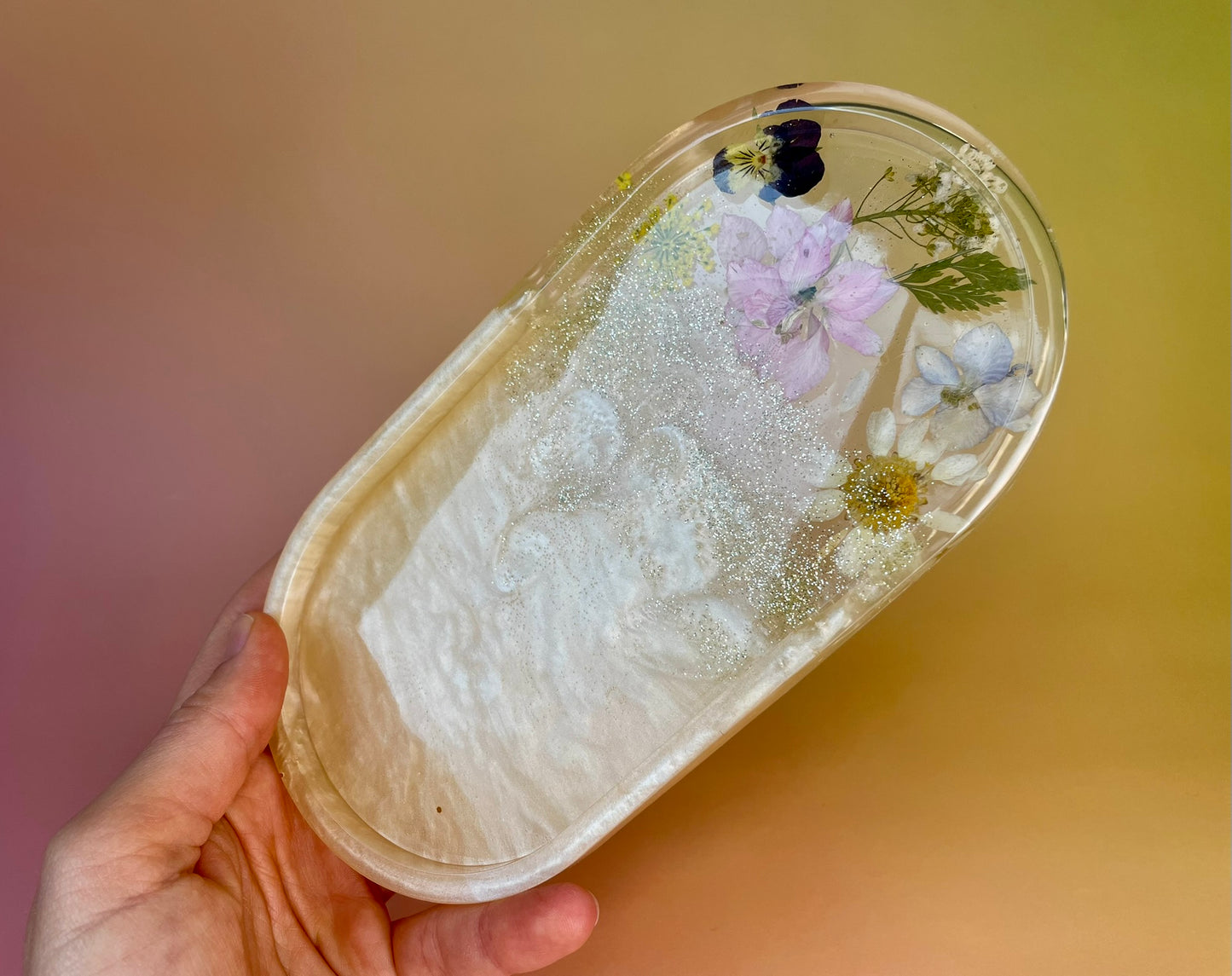 Kleines Tablett aus Epoxidharz in Champagne mit Glitzer und echten Blüten in der Hand gehalten