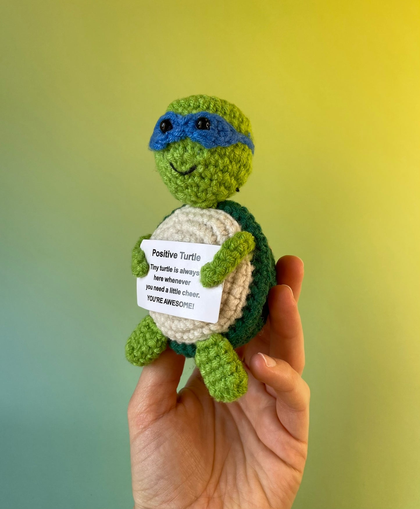 Positive Schildkröte mit blauer Augenmaske - gehäkelte Figur mit motivierender Botschaft in der Hand gehalten. In Ninja Stil.