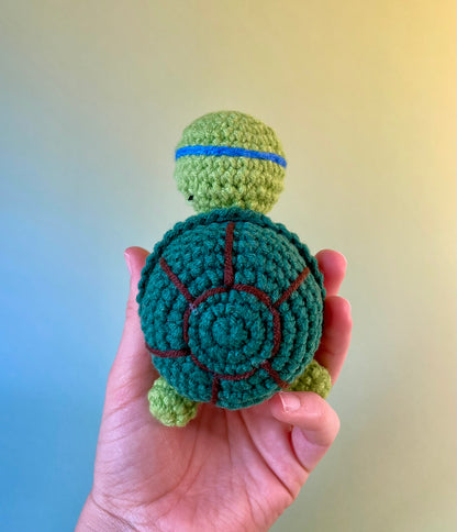 Positive Schildkröte - gehäkelte Figur mit motivierender Botschaft in der Hand gehalten von hinten fotografiert. In Ninja Stil.