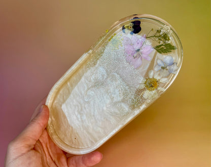 Kleines Tablett aus Epoxidharz in Champagne mit Glitzer und echten Blüten in der Hand gehalten 