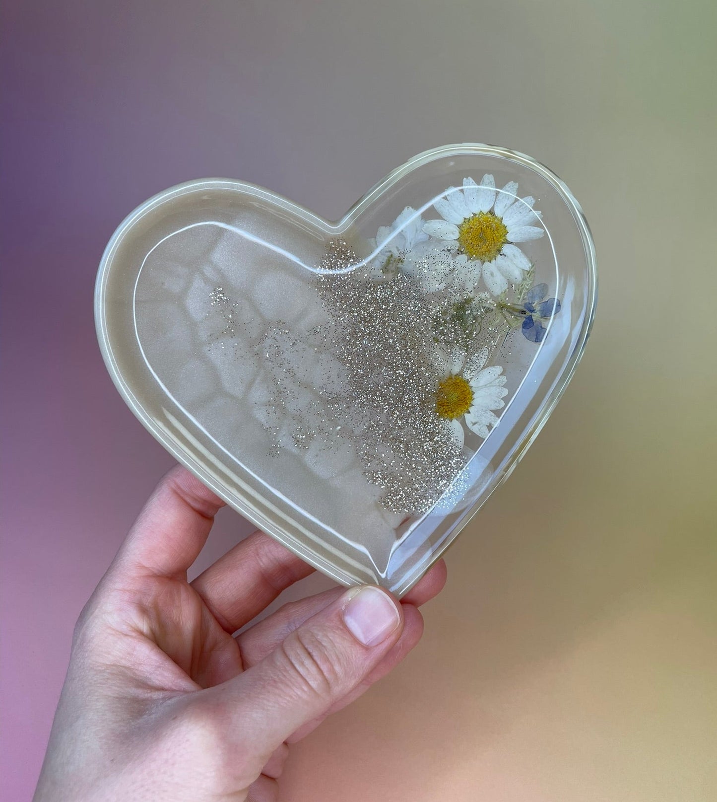 Herzförmiges Schälchen aus Epoxidharz mit echten Blumen in Beige in der Hand gehalten 