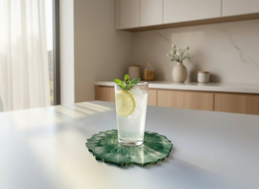 Einzelner Untersetzer - aus Epoxidharz, handgefertigt, in Grün-Gold, Rand Natur, in Verwendug mit einem kleinen Glas Wasser.