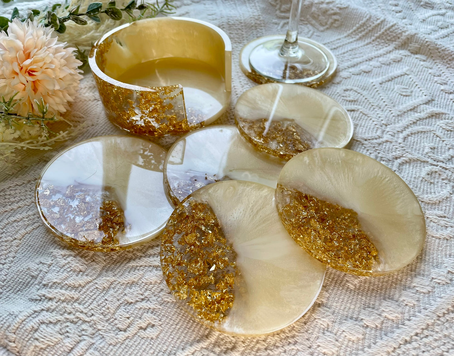 Handgefertigtes Epoxidharz Untersetzer Set 6er in Champagne mit Goldflocken - Luxuriöse Tischdeko mit Halter und Weinglas auf weißer Spitzendecke
