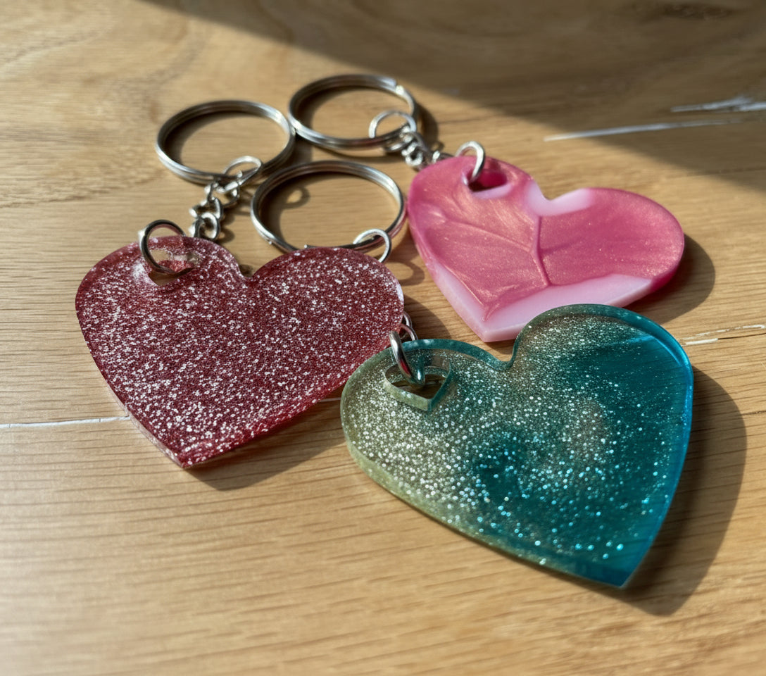 Drei Stück herzförmige Epoxidharz Schlüsselanhänger - in Rosa Glitzer, Rosa soft Glam, und Blau-Champage Farben.